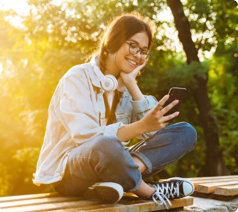 Eine junge Frau sitzt mit ihrem Smartphone auf einer Bank